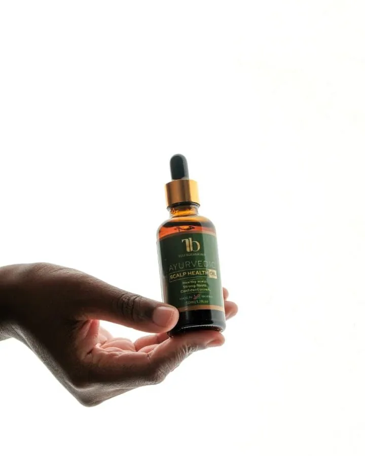 A hand holding the Tuli Botanicals oil bottle against a bright white wall.