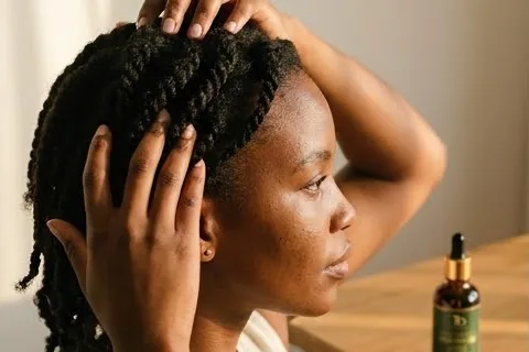 Oil being massaged into the scalp at the hairline, in warm light.