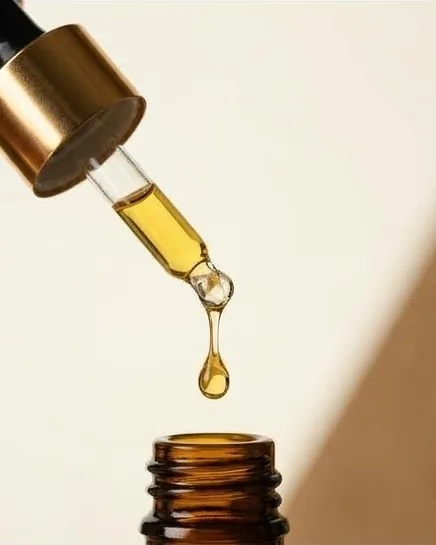 A single drop of golden oil falling from a glass dropper.